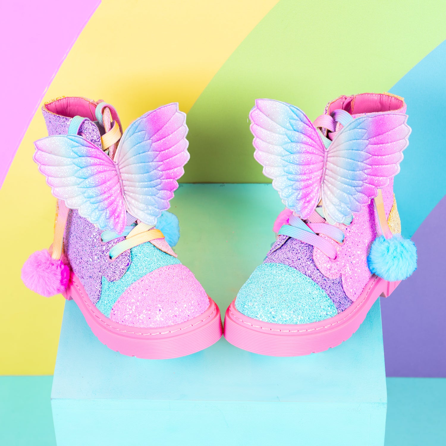 Colorful rainbow glitter boots with sparkly finish, butterfly wings, and playful pom pom laces.