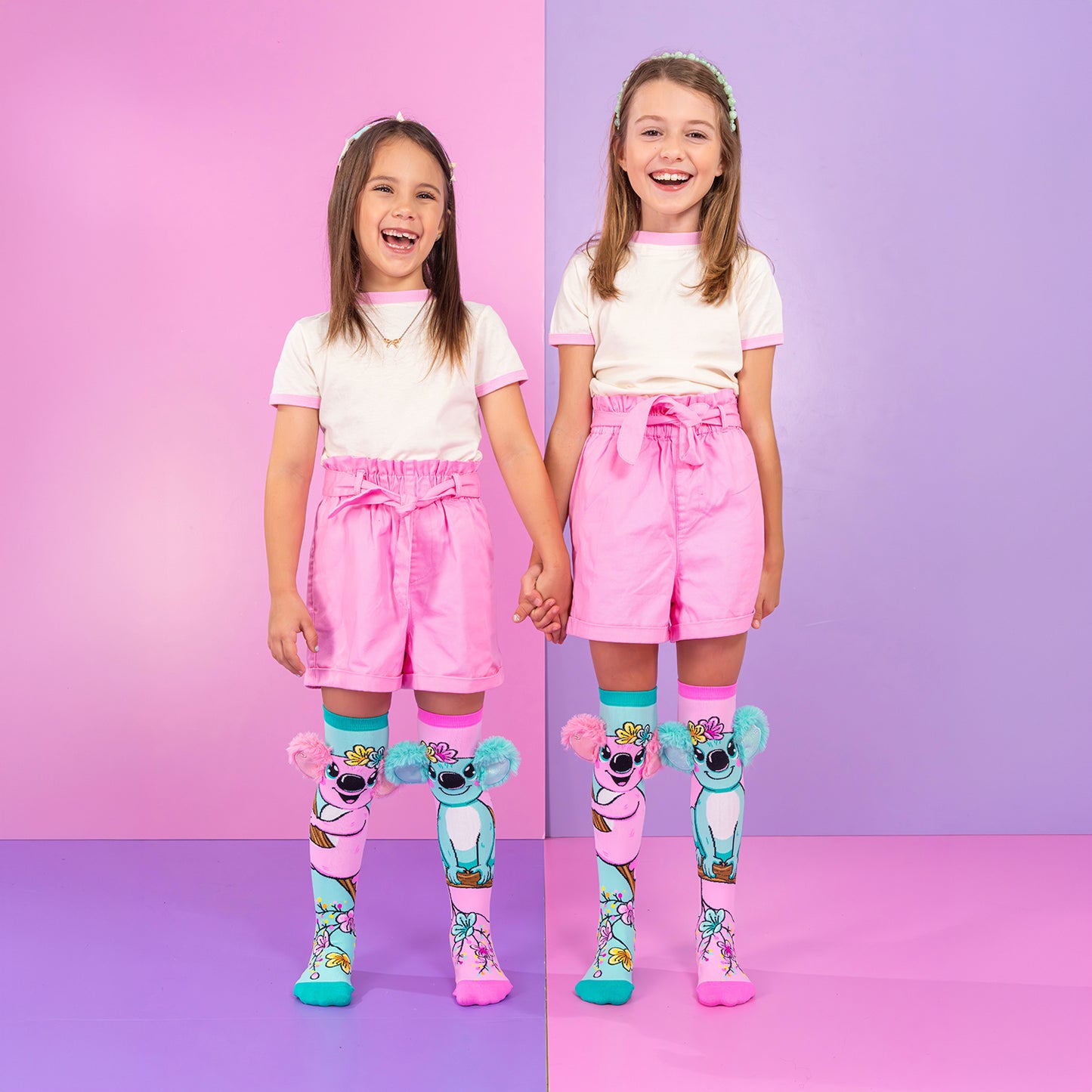 Two children wearing colorful koala knee high socks with plush ears and floral character artwork.