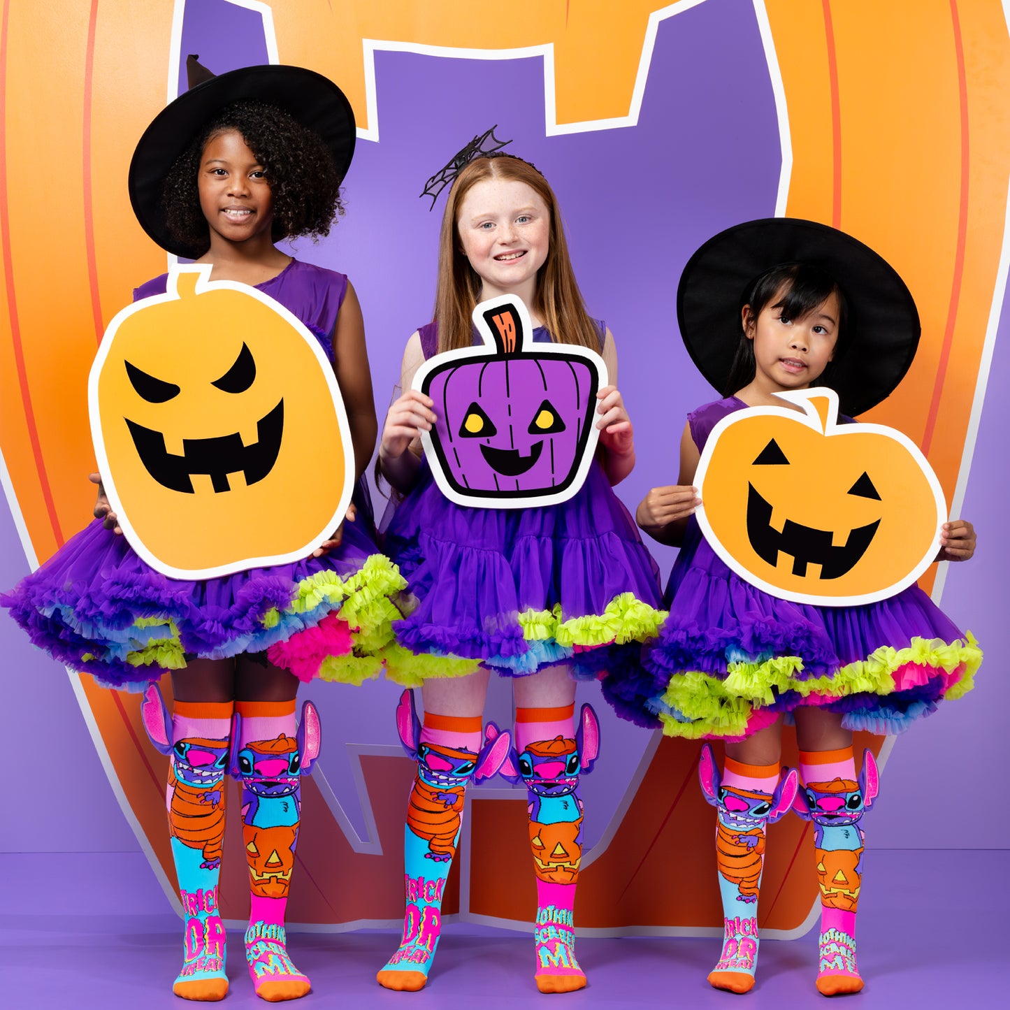 Kids wearing Disney Stitch Halloween socks with pumpkin props, witch costumes, and colorful trick or treat graphics.